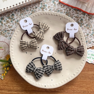 Three pairs of plaid bow hair ties in beige, brown, and monochrome on display card