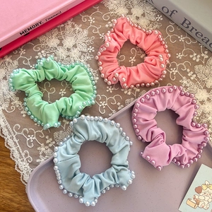 Detailed view of four pearl-edged scrunchies in pastel colors on a vintage tray