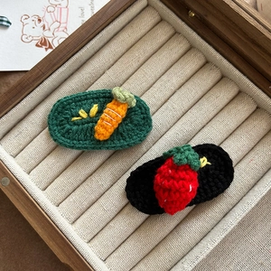 Handmade crochet strawberry and carrot hair clips for kids on a wooden jewelry display box