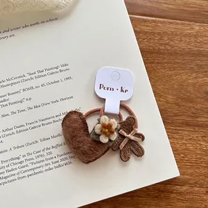 Detail van gebreide haarelastiek met bruin vilt hart, madeliefje en beer borduursel