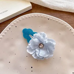 Detailed view of light blue fabric flower hair clip with rhinestone on ceramic plate