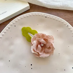 Close-up of fabric flower hair clip with rhinestone and green leaf in ceramic tray