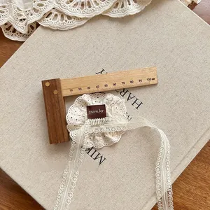 Detail of cream lace flower hair clip with dangling ribbons and brand tag on canvas