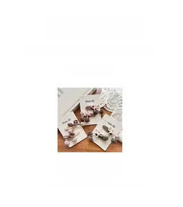 Détail de pinces à cheveux cerise en peluche marron, crème et vert sur cartes de support