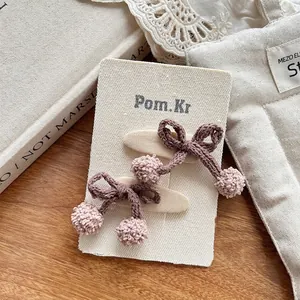 Détail de deux pinces à cheveux en laine tricotée marron et rose avec pompons