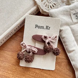 Détail de deux barrettes à cheveux cerises crochetées avec nœuds et pompons en peluche