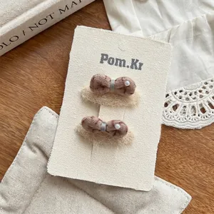 Détail de deux barrettes à nœuds à carreaux marron avec perles sur carte de présentation