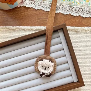 Detailed close-up of a plush lion charm with brown ribbon on a wooden jewelry display tray
