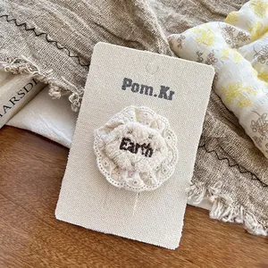 Dettaglio accessorio per capelli in pizzo beige con ricamo Earth su cartoncino