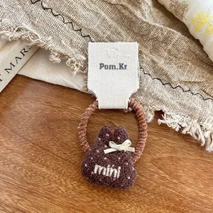 Dettaglio di un elastico per capelli con orsetto di peluche marrone e ricamo mini su tavolo