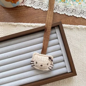 Close-up of a Hello Kitty style corduroy plush charm with brown hanging cord and bow
