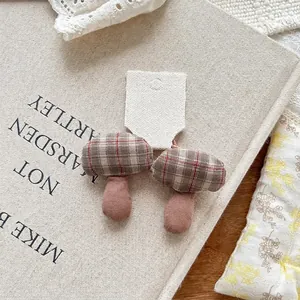 Detailed close-up of handmade checkered mushroom fabric hair clips on a book backdrop