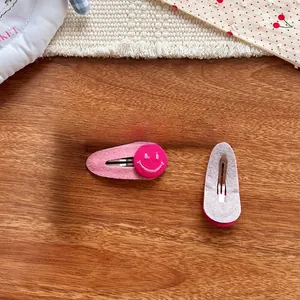 Détail de barrettes en feutre rose avec broderie smiley et structure de clip BB en métal