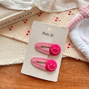 Détail de pinces à cheveux à nœud rose avec broderie smiley rouge sur base en tissu