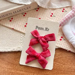 Paire de barrettes à cheveux à nœud en tissu écossais rouge sur carte sur une table en bois