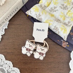 Dettagli di elastici per capelli con orsetti ricamati color crema e fiocchi marroni morbidi