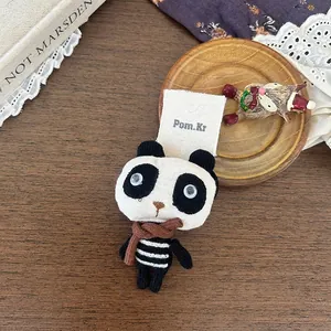 Détail d'un accessoire en peluche panda tricoté avec écharpe brune sur carte Pom.Kr
