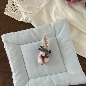 Detailed view of striped fabric bunny brooch with a dark polka dot bow on a soft blue cushion