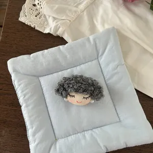 Detail of a handmade cartoon character brooch with curly grey yarn hair and pearl earring