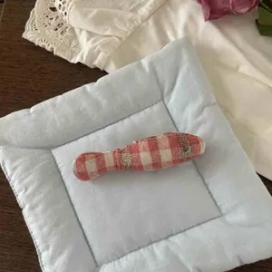 Close-up of a handmade red checkered stuffed fish brooch and a blue quilted padded mat