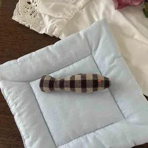 Detail of cute checkered fabric fish brooch accessory on a soft blue quilted mat