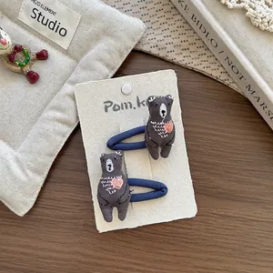 Détail de deux pinces à cheveux en tissu ours avec broderie cœur rose sur carte