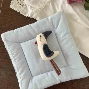 Detailed view of a handmade fabric coaster featuring a 3D stuffed bird doll on wooden table