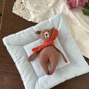 Detail of a brown stuffed fabric bear doll with orange scarf on blue quilted cushion