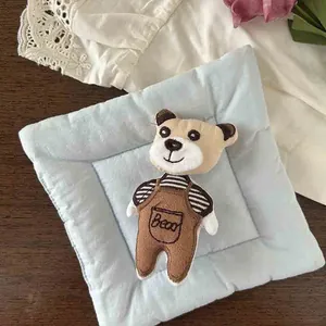 Detail of cute teddy bear plush brooch in brown overalls on light blue quilted mat