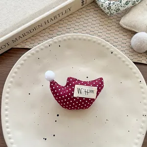 Dettaglio della spilla in tessuto bordeaux a pois con pompon di peluche bianco