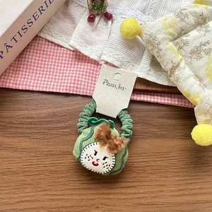 Detail of green knitted hair tie with cute cartoon face and red plaid bow decoration