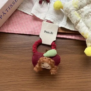 Close-up of a red fabric hair scrunchie with a cute plush doll on a wooden surface