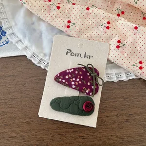 Détail d'un lot de barrettes à fleurs avec nœud vert et rose sur carton blanc