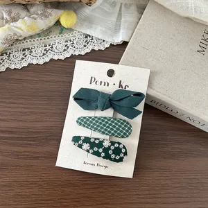 Détail de pinces à cheveux en tissu vert foncé avec broderie florale et nœud classique