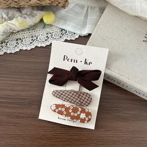 Lot de trois barrettes à cheveux en tissu brodé et nœud en velours sur carte de présentation