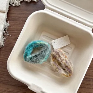 Détail de deux chouchous en maille duveteuse bleu et marron dans une boîte en papier