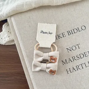 Detailed embroidery of brown bear on beige linen bow hair ties for children