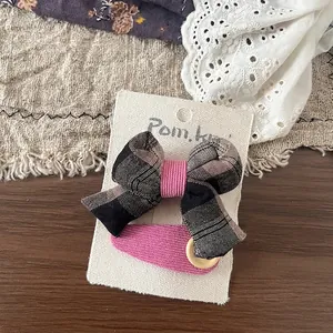 Détail d'une pince à nœud quadrillé et d'un clip BB en tissu rose sur carte