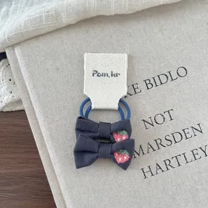 Detail of embroidered strawberry bows on navy blue high-elasticity hair ties for kids