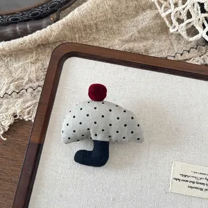 Detailed view of grey polka dot fabric umbrella brooch with a red fuzzy ball accessory