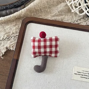 Close-up of a handmade red checkered umbrella-shaped fabric brooch with a plush pom pom