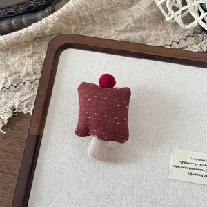 Detail of red fabric mushroom brooch with polka dots and pom-poms on linen background