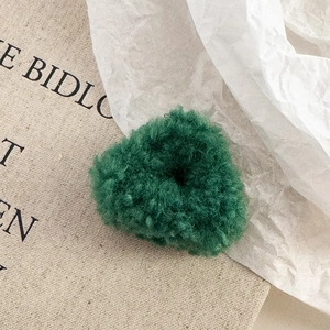 Gros plan d'une pince à cheveux en laine d'agneau vert foncé à texture pelucheuse douce