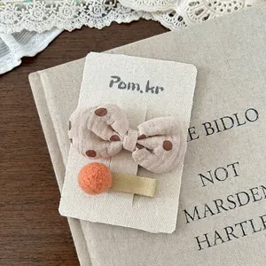 Detail von beige gepunkteter Schleifen-Haarklammer und orangefarbenem Filzball