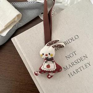 Close-up of cute white fabric rabbit keychain with red floral apron and embroidery details