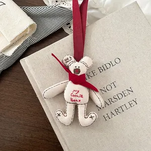 Detail of a beige linen teddy bear charm with a red scarf and My Cookie Bear embroidery