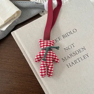Detail of red and white checkered cloth bear charm with green scarf on a linen book