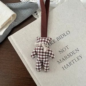 Detailed close-up of retro plaid bear charm with jute bow on minimalist fabric book