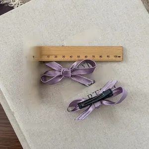 Detail view of two purple ribbon bow hair clips with black metal alligator base