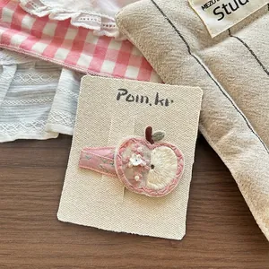 Close-up of handmade embroidered apple hair clip with floral ribbon wrap details